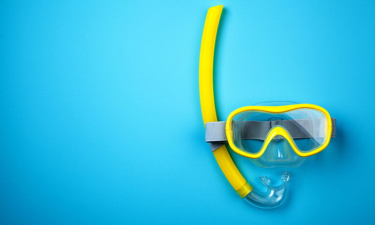 Un tube respiratoire jaune et des lunettes de plongée sur un fond bleu clair, avec beaucoup d'espace libre à gauche.