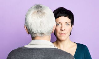 Une femme fait face à une personne âgée, dos au spectateur, sur un fond violet