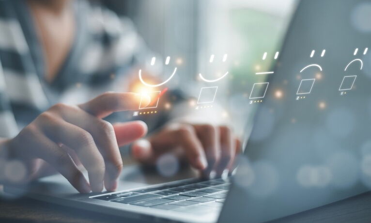Zwei Hände bedienen Laptop, darüber digitale Bewertungs­skala mit markiertem positiven Feedback‑Symbol.