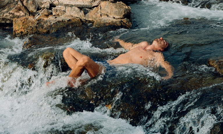 Person liegt in einem Wildbach zwischen Felsen und lässt sich vom Wasser umspülen.